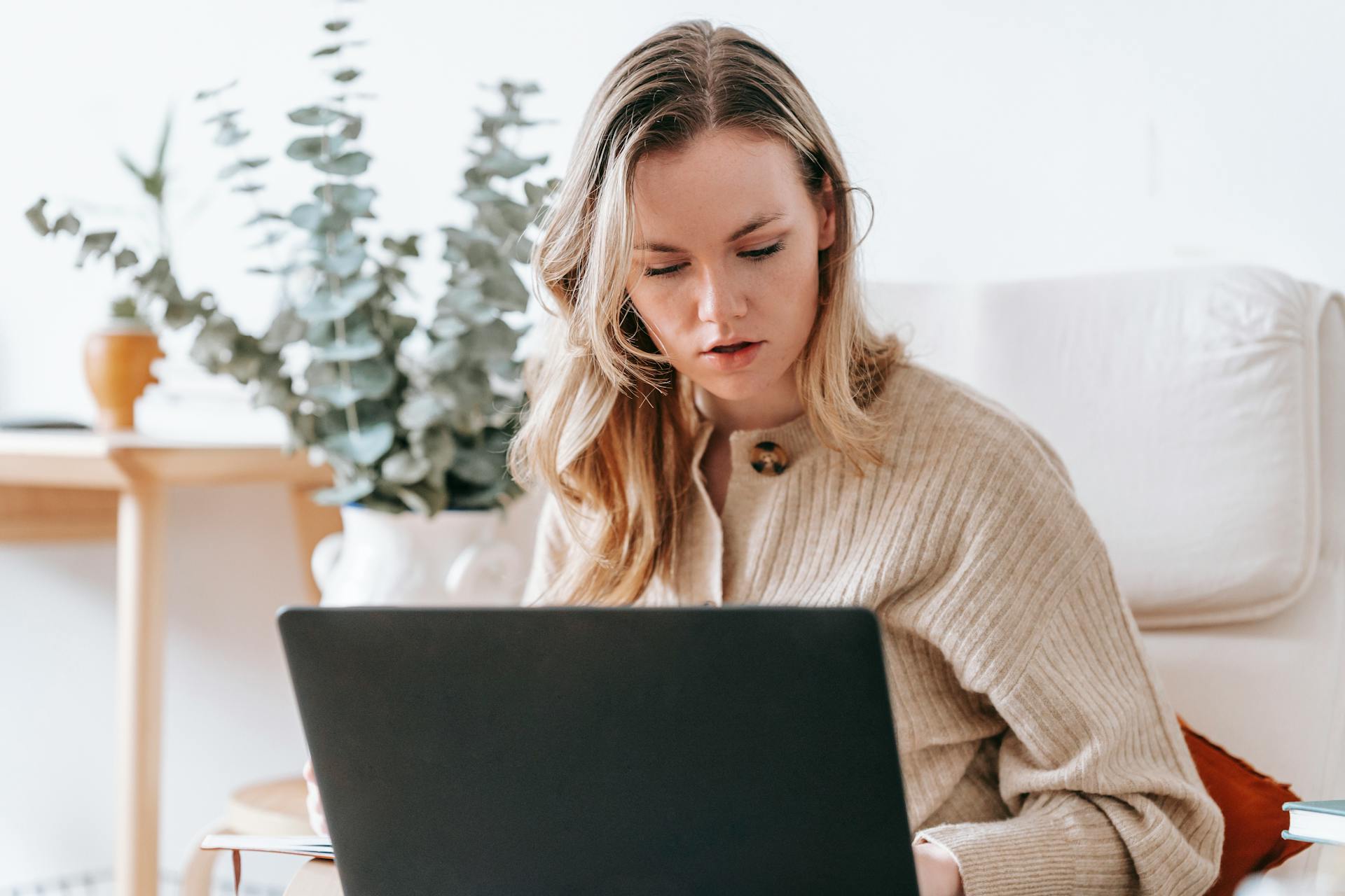 Serious female remote specialist working online on netbook on blurred background of interior of lounge