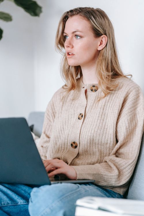 Free Concentrated intelligent female in beige woolen cardigan working distantly with netbook and looking away while pondering Stock Photo