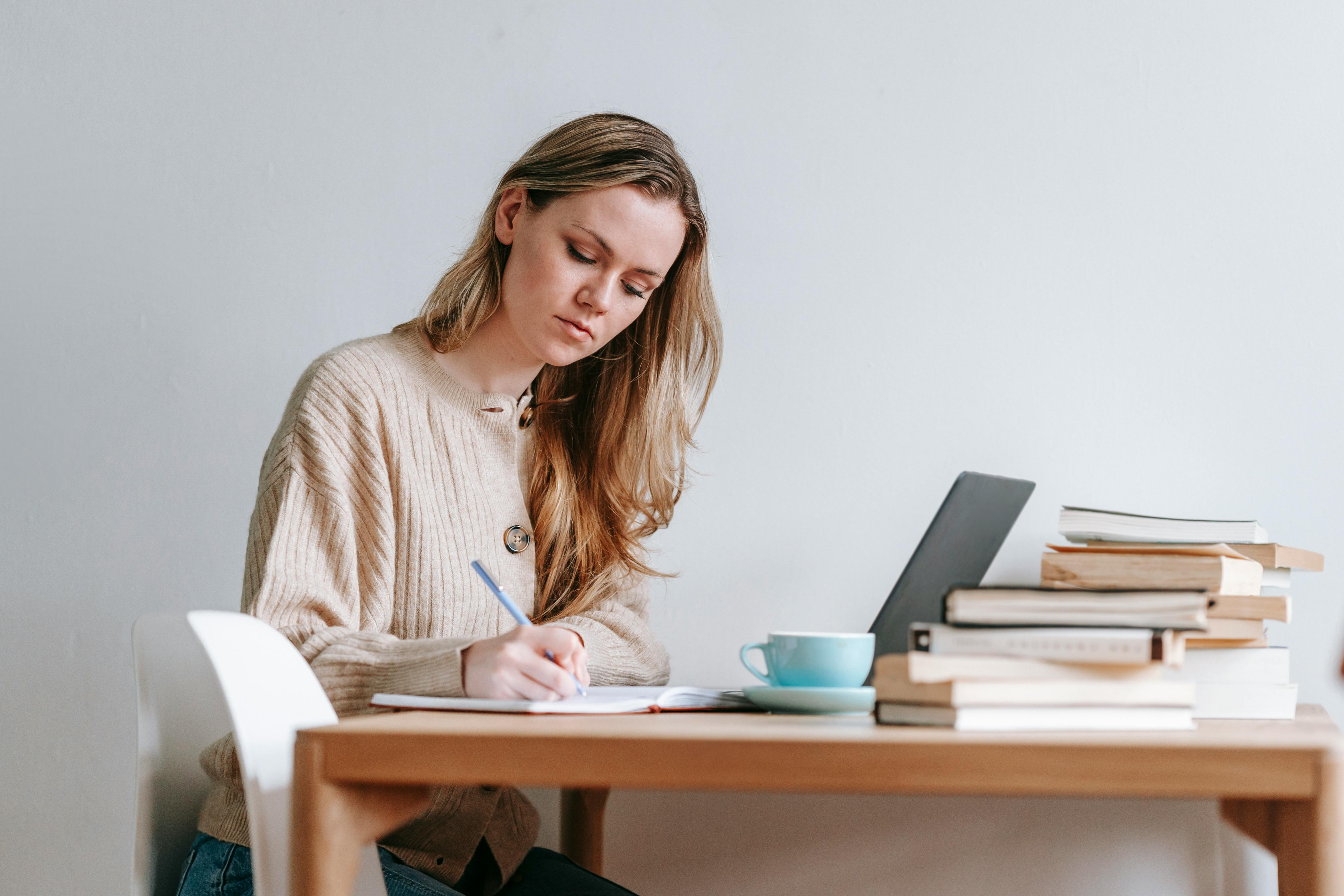 serious woman writing ideas in notebook near laptop and books