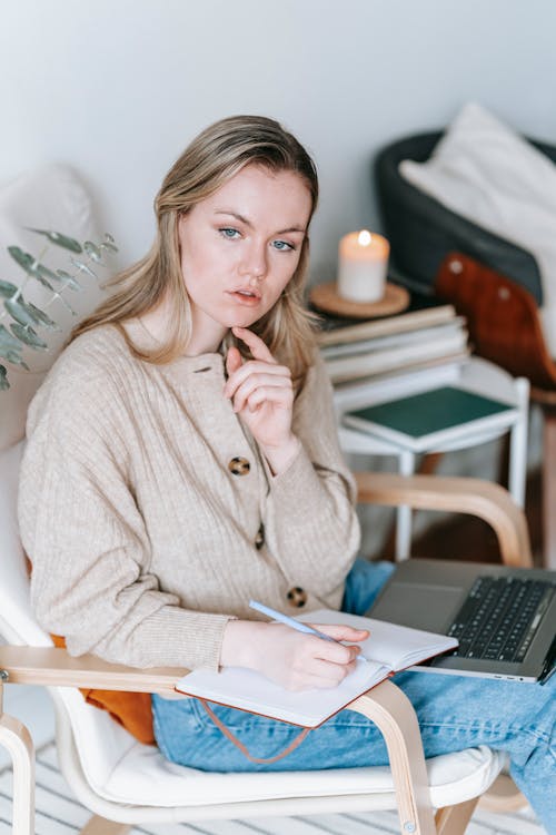 Focused businesswoman writing in notebook near shiny candle and laptop