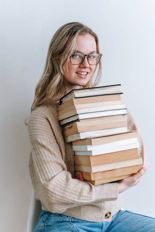 Smart happy student in eyeglasses with pile of books