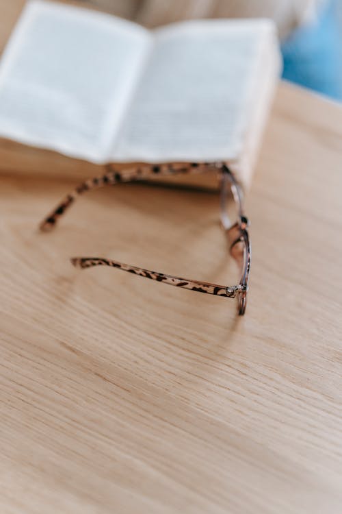 Free From above of stylish eyeglasses placed near interesting book near timber beige table on blurred background Stock Photo