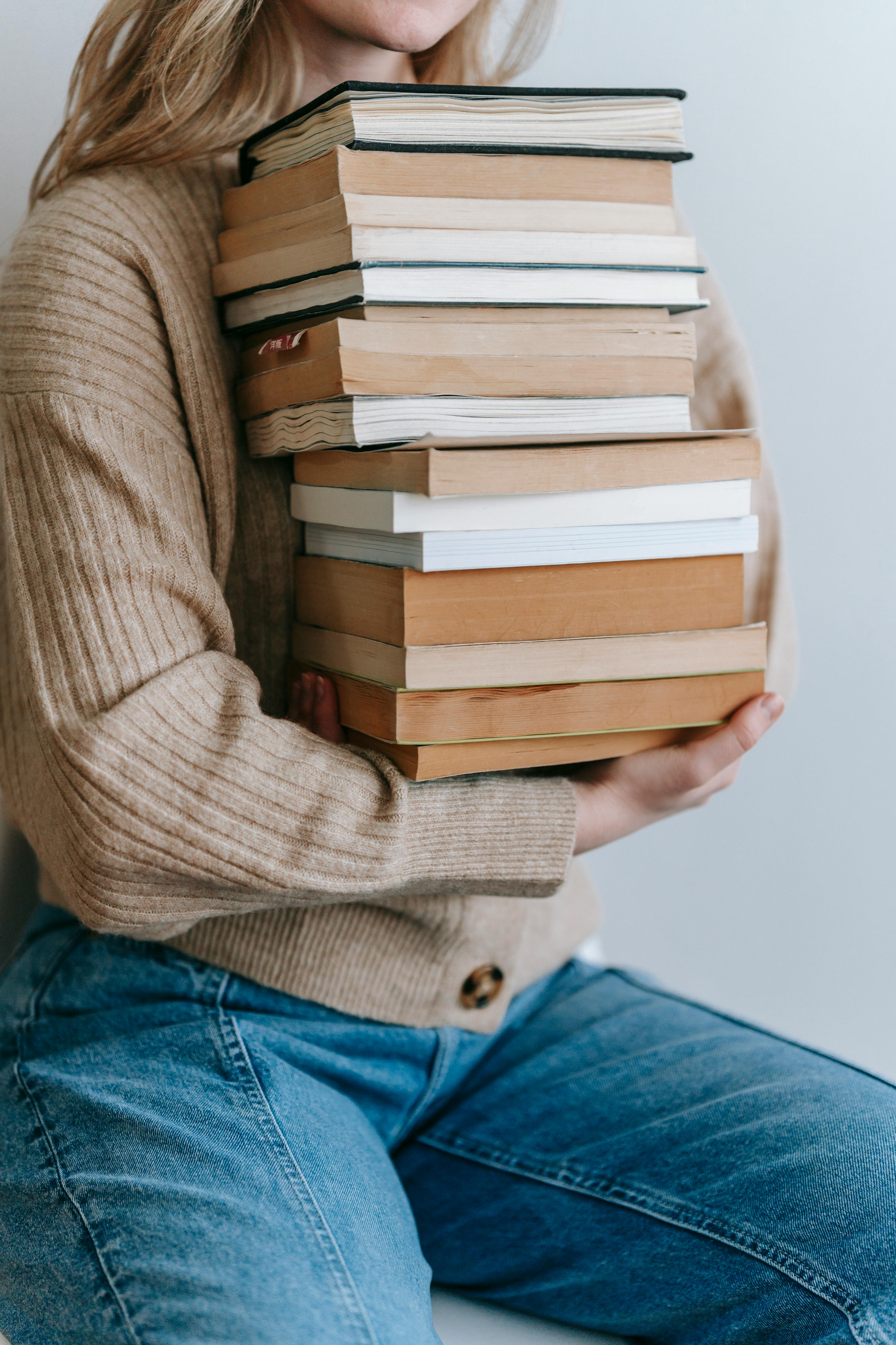 Free Crop unrecognizable female student in casual clothes holding stack of books against light wall in daytime Stock Photo