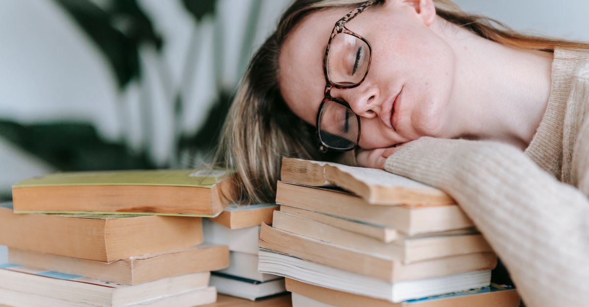 student sleeping on a pile of textbooks with a peaceful expression