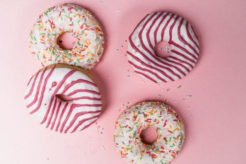Free Colorful donuts with icing and sprinkles on a pink background, perfect for dessert lovers. Stock Photo
