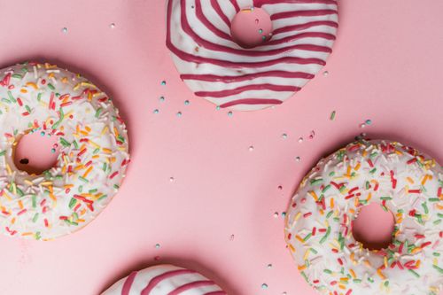 Free Brightly decorated donuts with icing and sprinkles on a pink background from above. Stock Photo