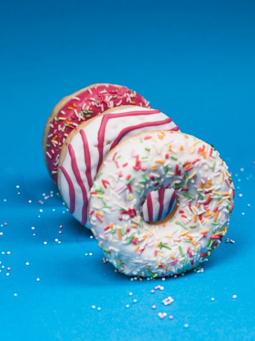 Free Three colorful sprinkled donuts stacked on a vibrant blue backdrop for a tasty treat visual. Stock Photo