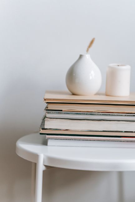 Collection of books with white vase and candle placed on round table on white background