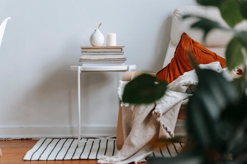 Free Comfortable light room with armchair with cushion and plaid near small table with stack of books and ceramic vase Stock Photo