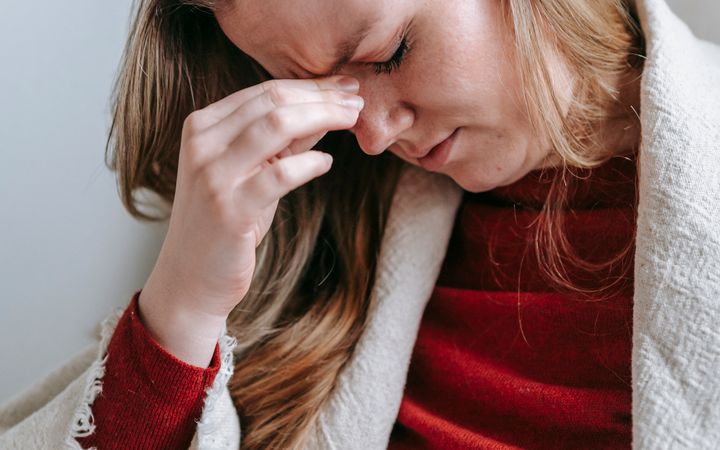 Upset serious young female with long blond hair in casual clothes touching forehead with closed eyes while resting in armchair at home