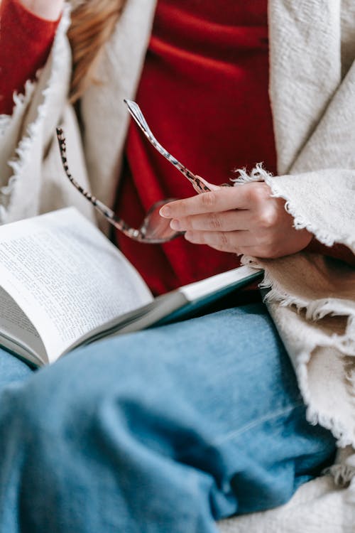 Free Crop anonymous lady resting on couch with book on knees in daylight Stock Photo