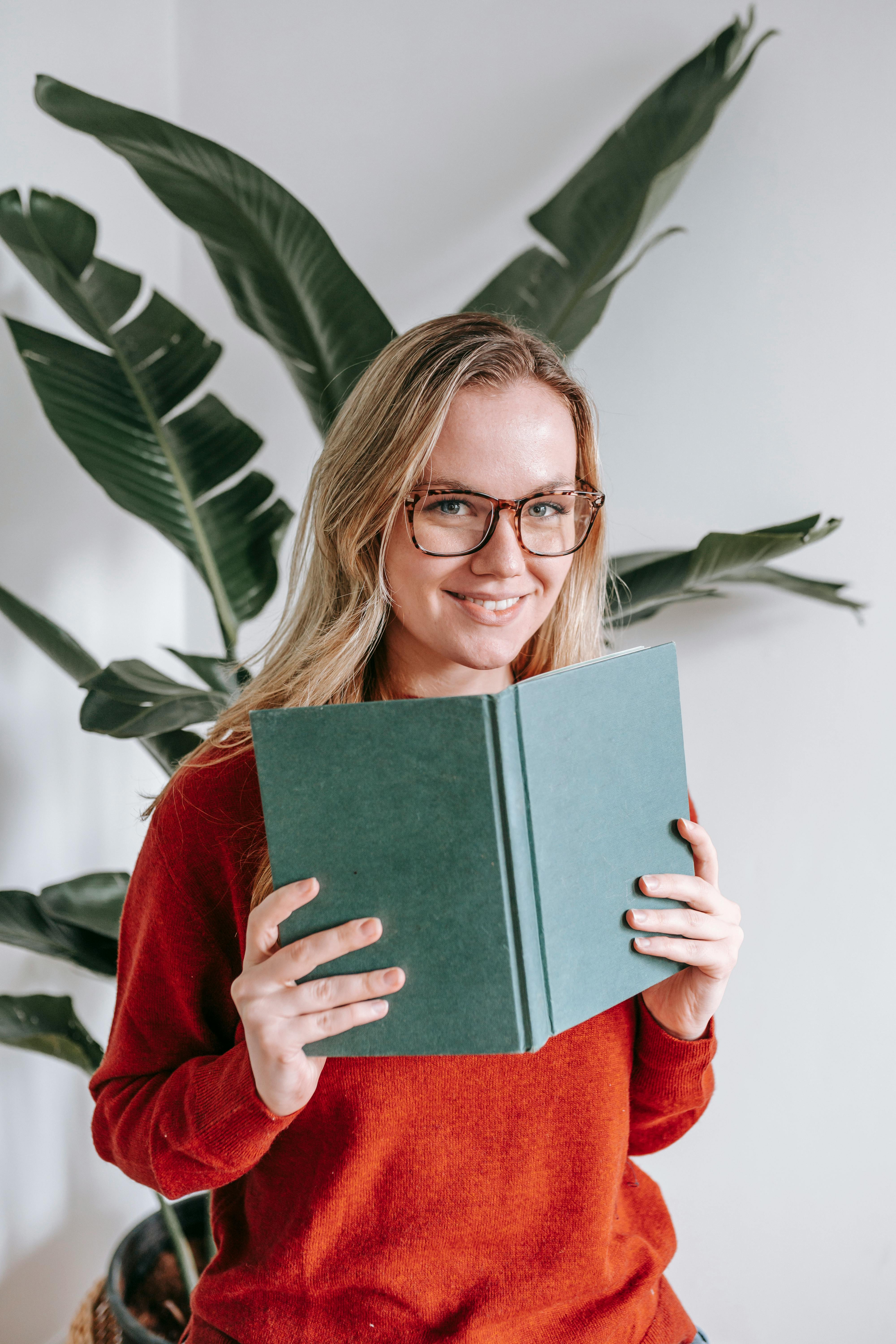 delighted young lady smiling while reading book in light room