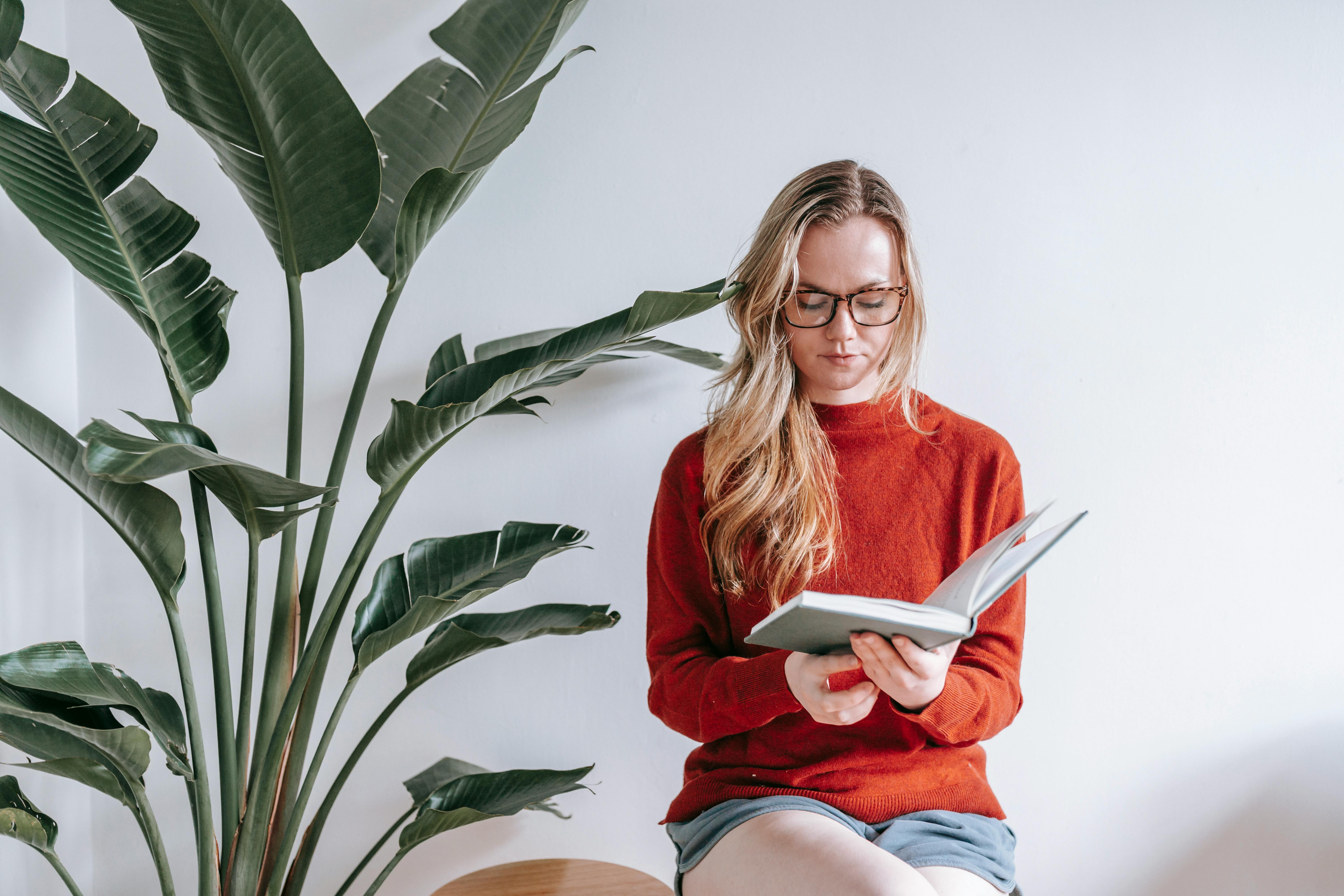 clever young lady reading textbook sitting near white wall at home