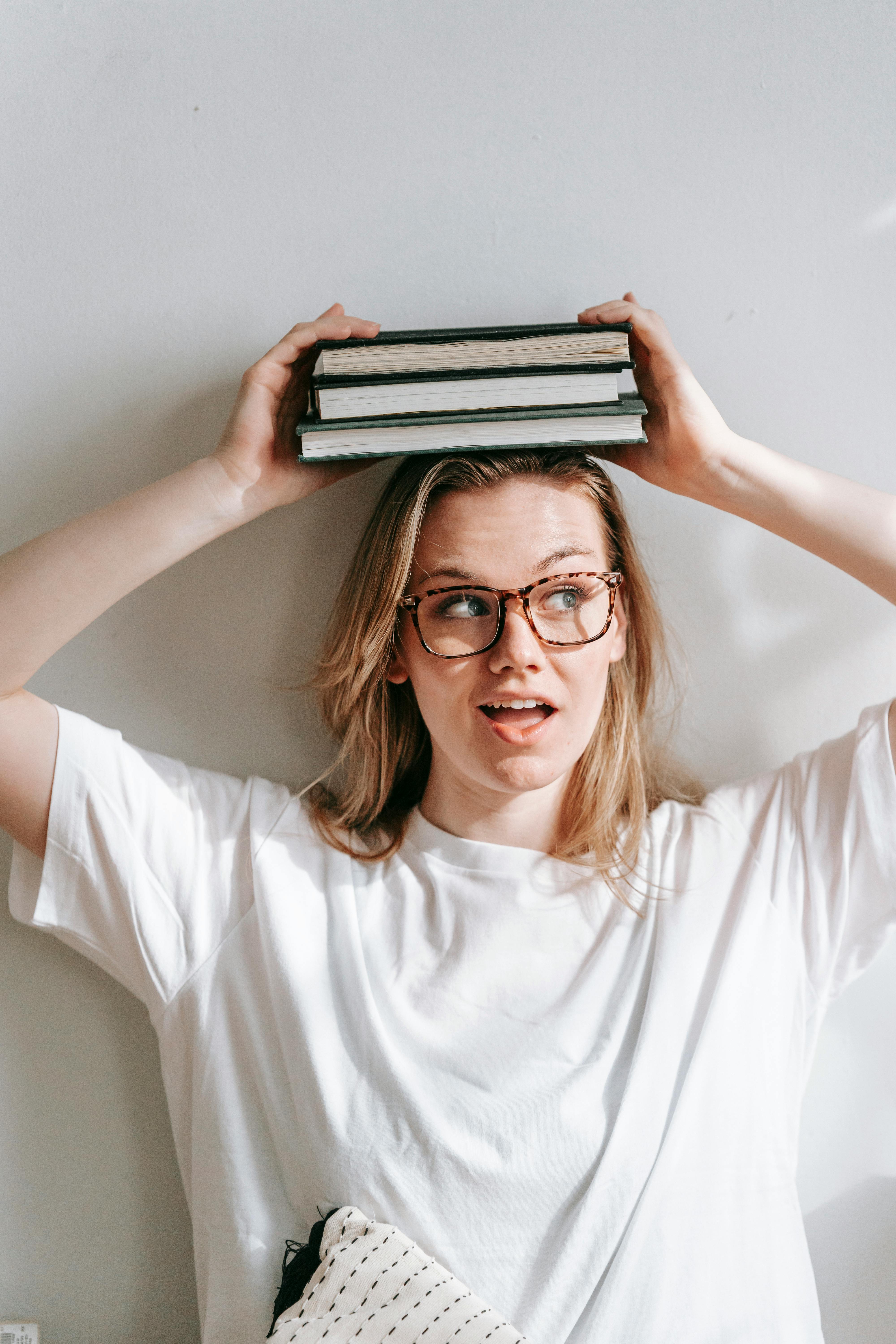 positive woman with books on head near wall