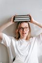 Positive woman with books on head near wall
