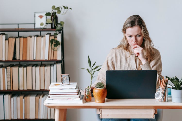 Pensive Woman Browsing Laptop Near Books