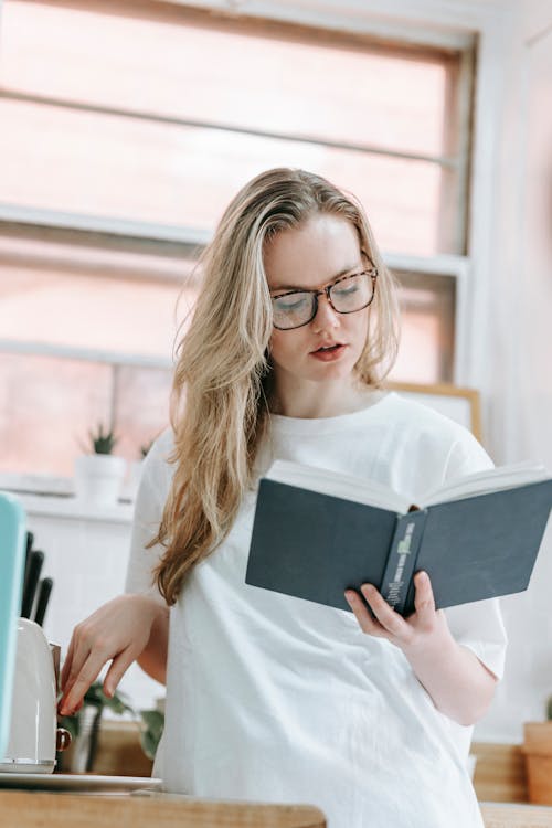 Free Focused woman reading book in kitchen Stock Photo