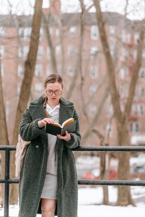 Focused woman reading book on snowy street