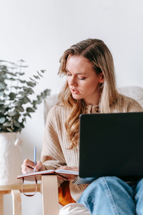 Free Young woman with laptop writing in notebook Stock Photo