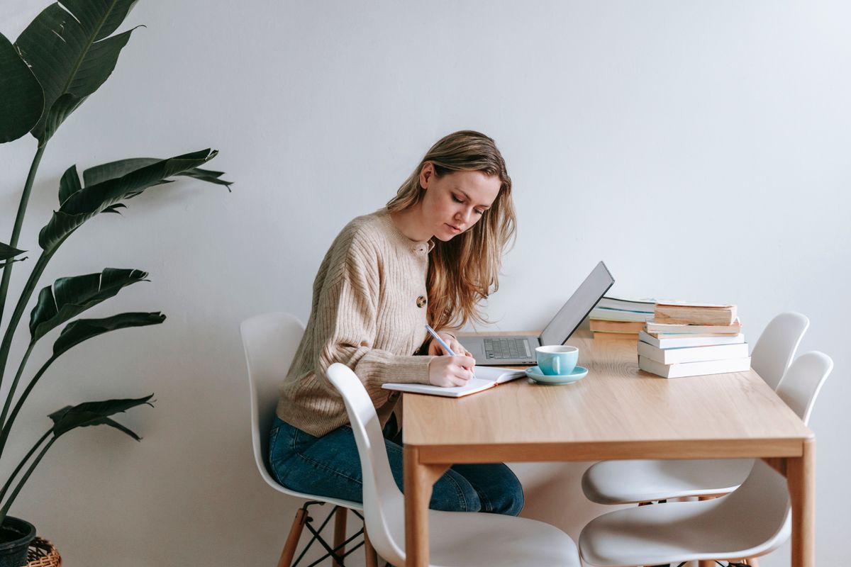 Focused woman writing a marketing strategy in a notebook beside her laptop