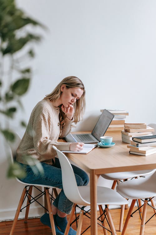 Focused woman writing in notebook near laptop