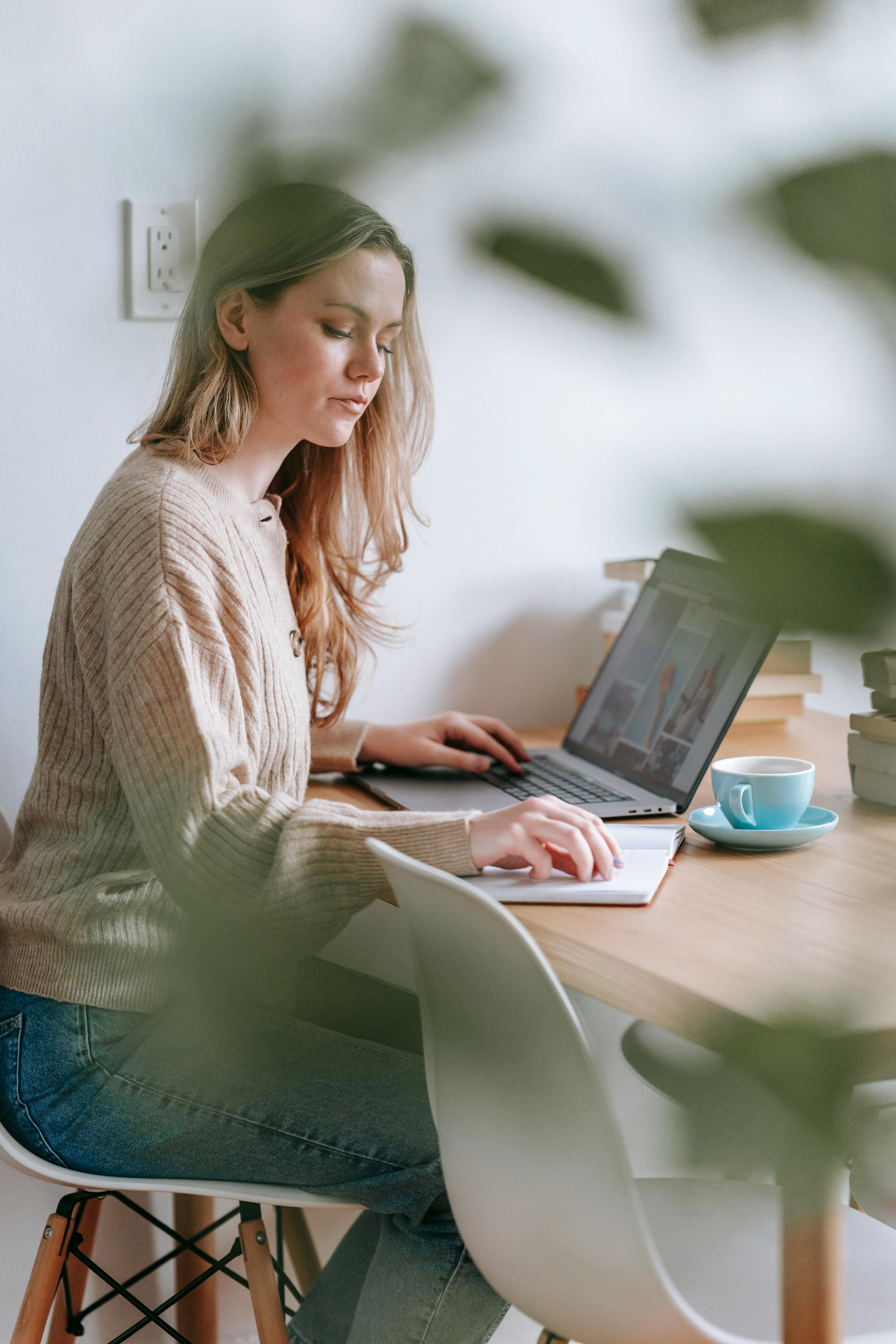 pensive woman working at table with laptop and notebook