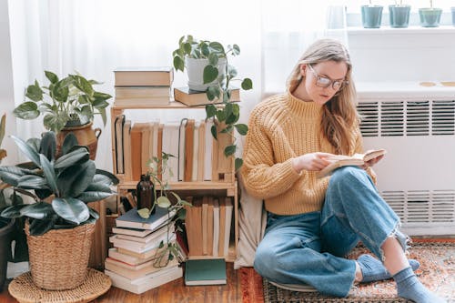 A Woman Sitting Near the Bookshelf with Potted Plants