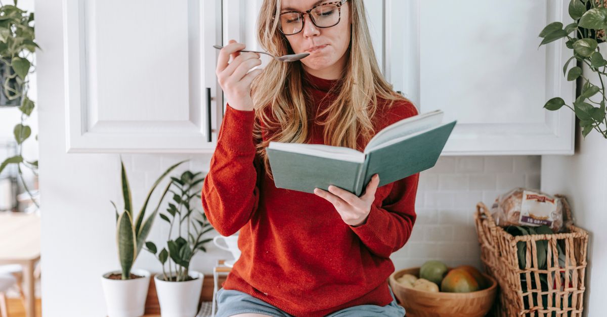 Reading Eating A Woman Eating while Reading a Book in the Kitchen · Free Stock Photo