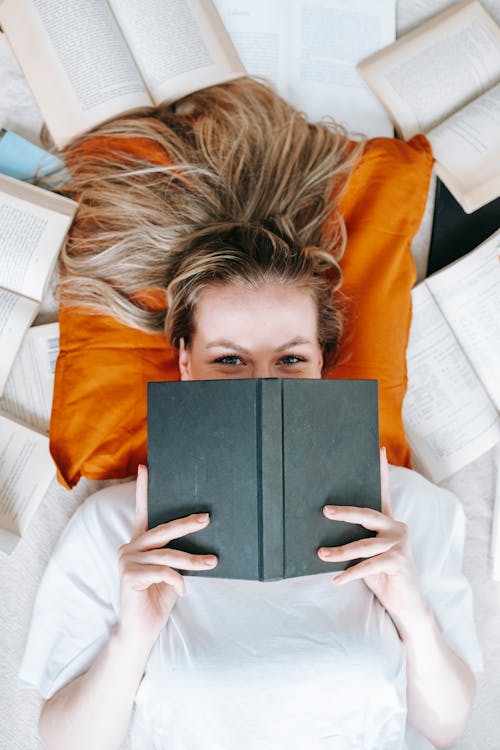 A Woman Lying on Bed and Covering her Face while Holding a Book · Free ...