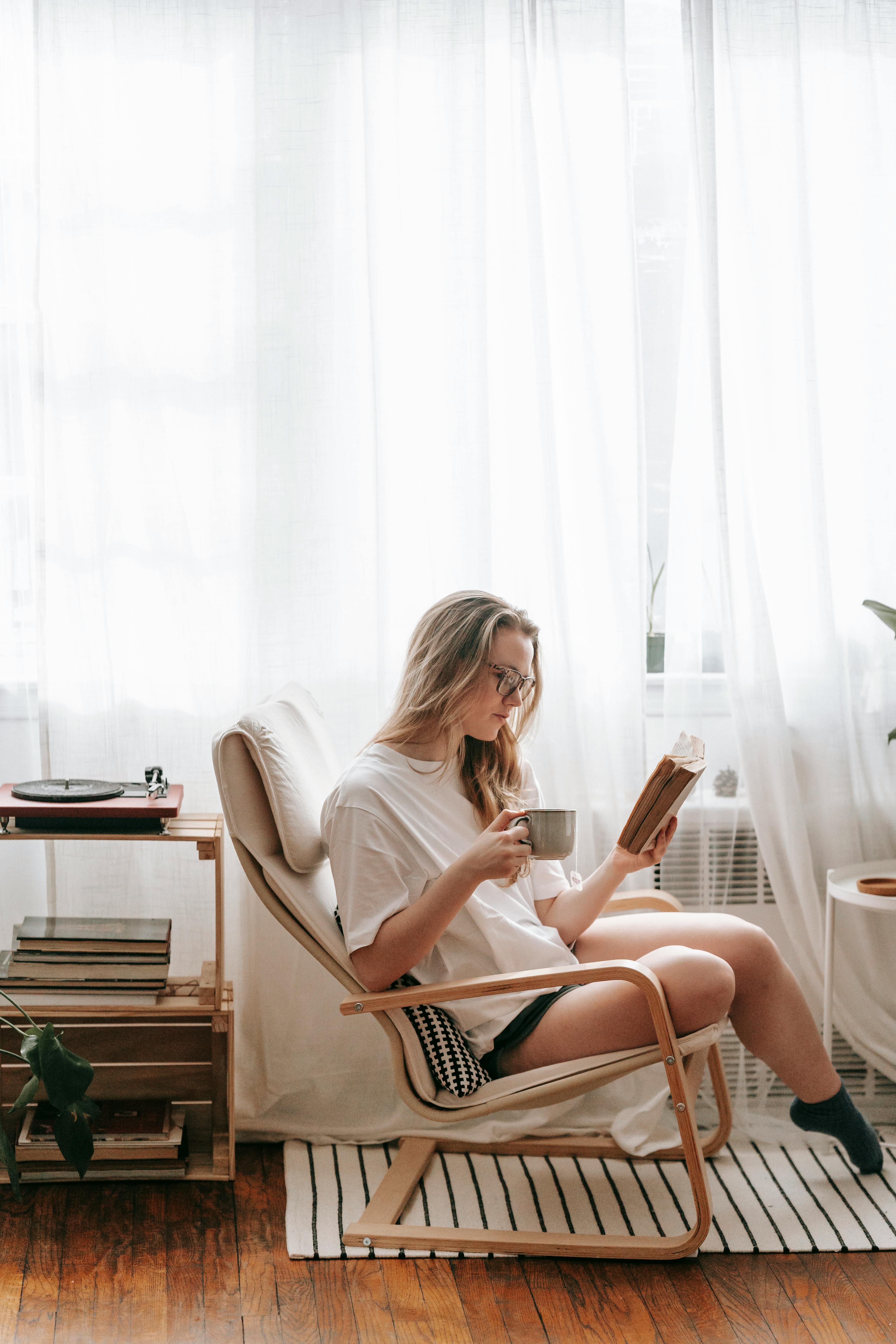 a woman in a white shirt reading a book while drinking coffee