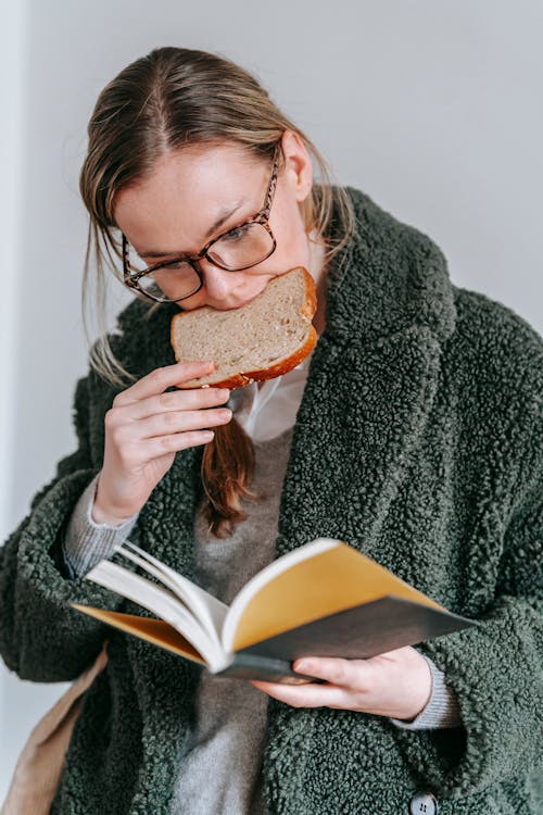 Woman Reading Book while Eating Bread