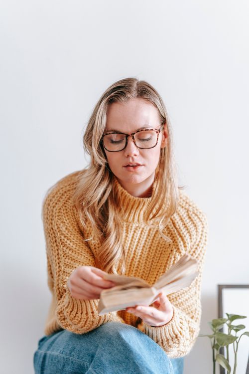 Free A woman in a knitted sweater enjoys reading a book indoors. Stock Photo