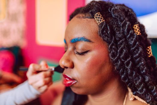 Close-up of a model with vibrant makeup being applied, highlighting bold colors and unique hairstyle.