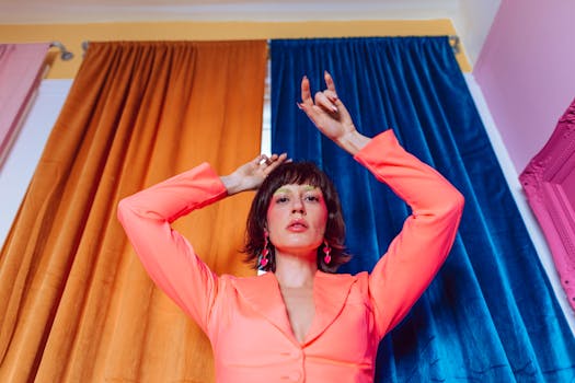 A fashionable woman poses indoors with brightly colored background drapes.