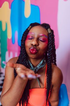 A young woman with colorful makeup blows a kiss against a vibrant background.