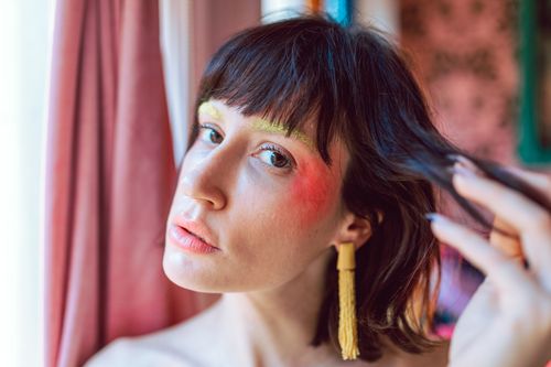 Free Artistic close-up portrait of a woman with colorful makeup and tassel earrings in soft lighting. Stock Photo