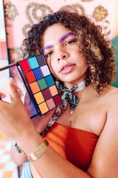 Young woman holding a colorful makeup palette, showcasing vibrant fashion and style.