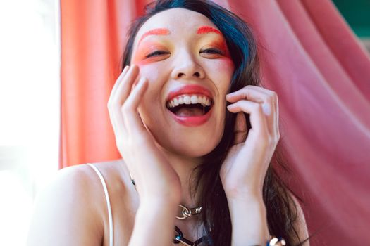 Close-up of a smiling woman with colorful artistic makeup indoors.