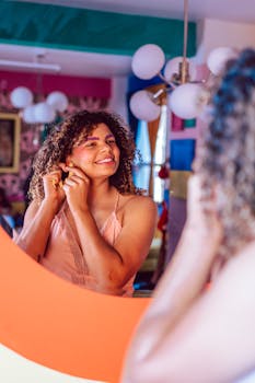 A young woman with curly hair smiling at her reflection in a colorful room.