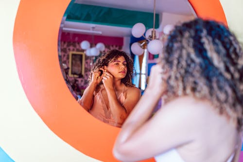 A Woman Wearing an Earring while Looking at a Mirror