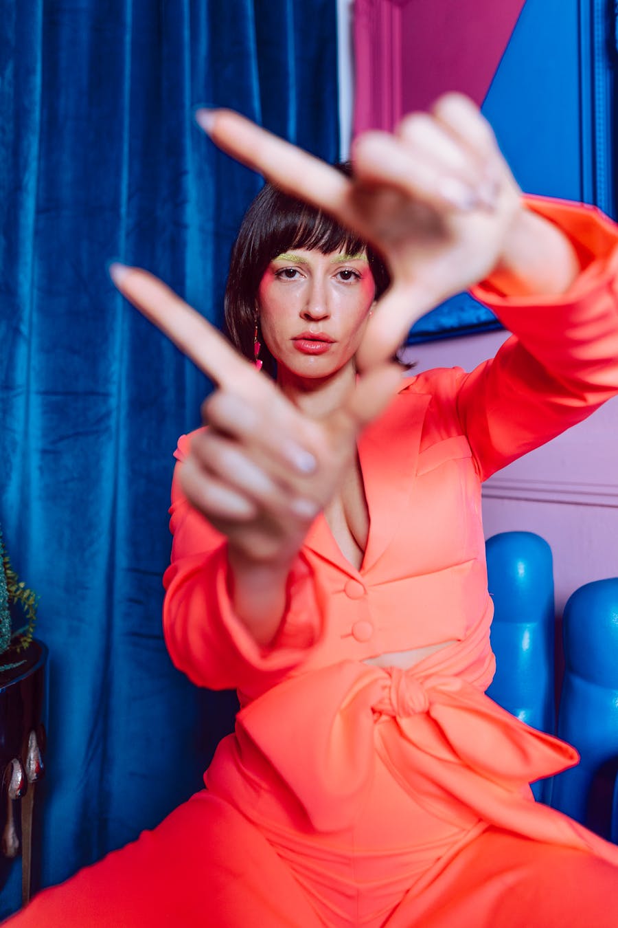 Colorful portrait of a stylish woman posing indoors with a vivid blue and pink backdrop.
