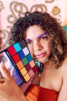 Portrait of a young person holding a colorful makeup palette indoors, showcasing vibrant style.