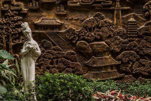 Free Exquisite stone statue in a traditional Chinese garden setting, surrounded by foliage and cultural architecture. Stock Photo