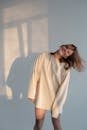 Happy young female in white sweatshirt smiling and shaking hair while dancing against gray wall