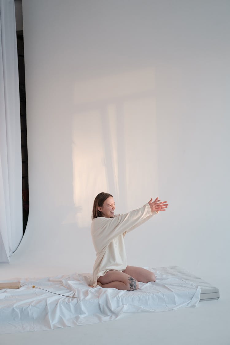 Happy Woman Sitting On Mattress And Touching Sunlight