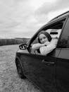 Grayscale Photo of Woman in the Car Window