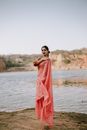 Full body of young Indian female wearing traditional red sari dress standing on sandy shore of lake
