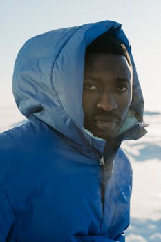 A man in a blue jacket stands outdoors in a winter landscape, exuding a calm and introspective gaze.