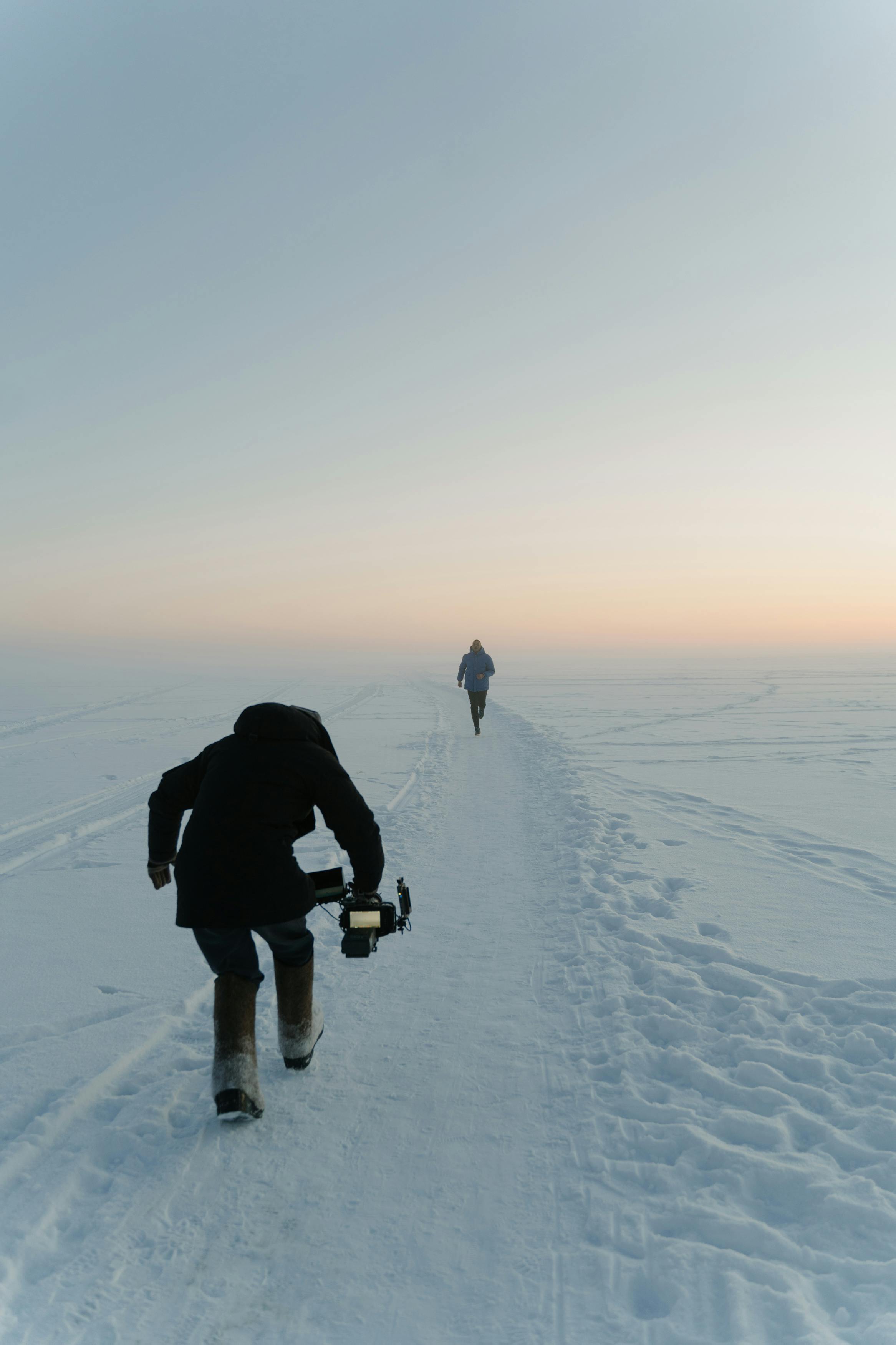 a videographer taking video of a person running on a snow covered ground