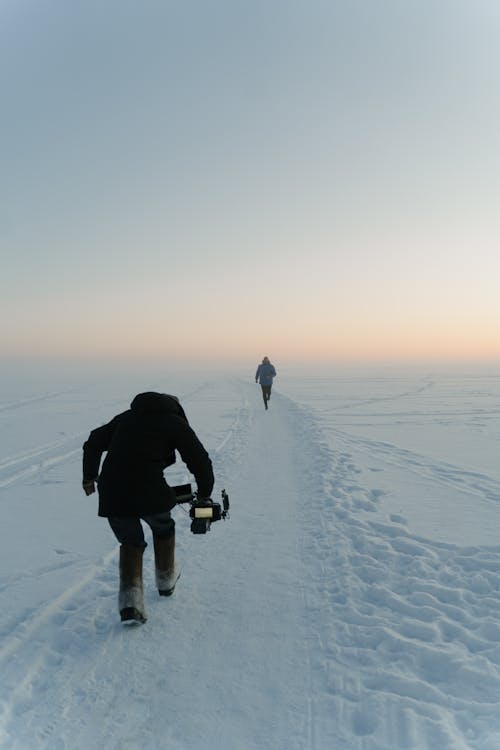 A Videographer Taking Video of a Person Running on a Snow Covered Ground